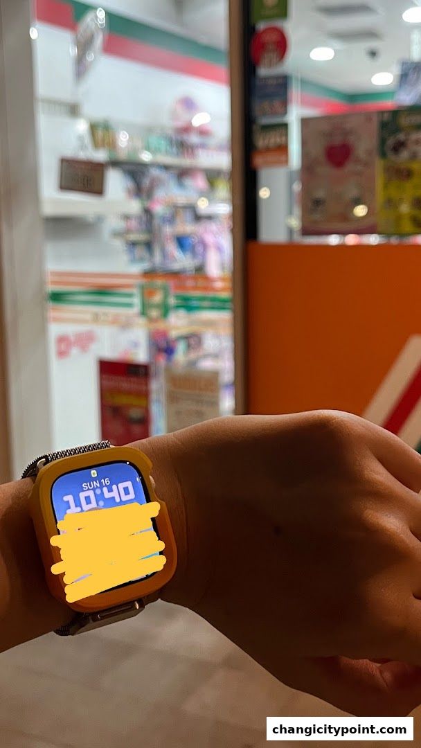 A person's wrist wearing a smartwatch in front of a 7-Eleven store.