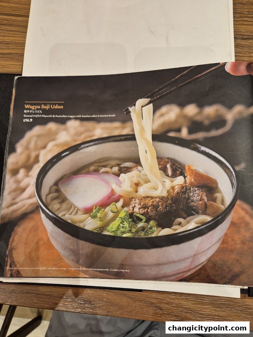 A close-up of a Wagyu Suji Udon dish with noodles and meat in broth.