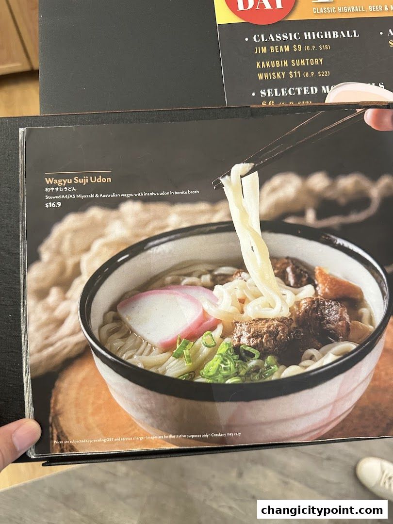 A close-up of a Wagyu Suji Udon dish with chopsticks lifting noodles.