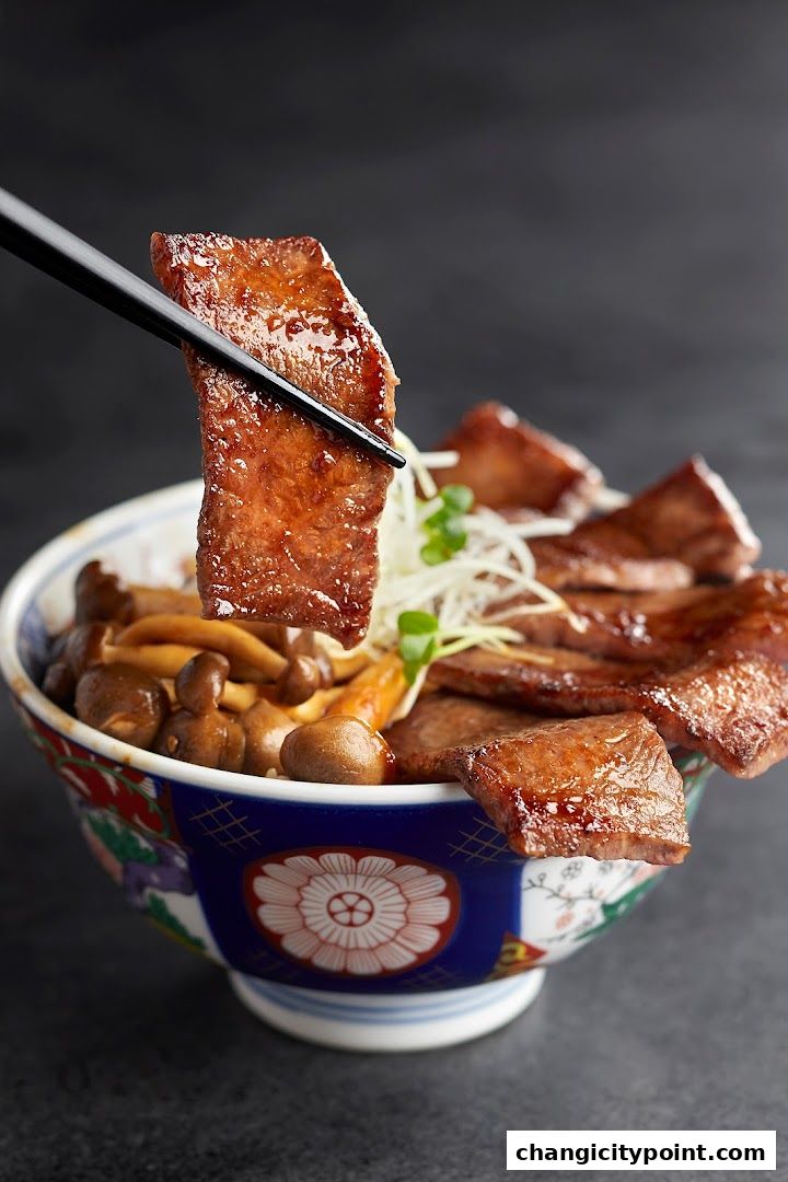 A close-up of a bowl of rice topped with grilled meat and mushrooms, held by chopsticks.