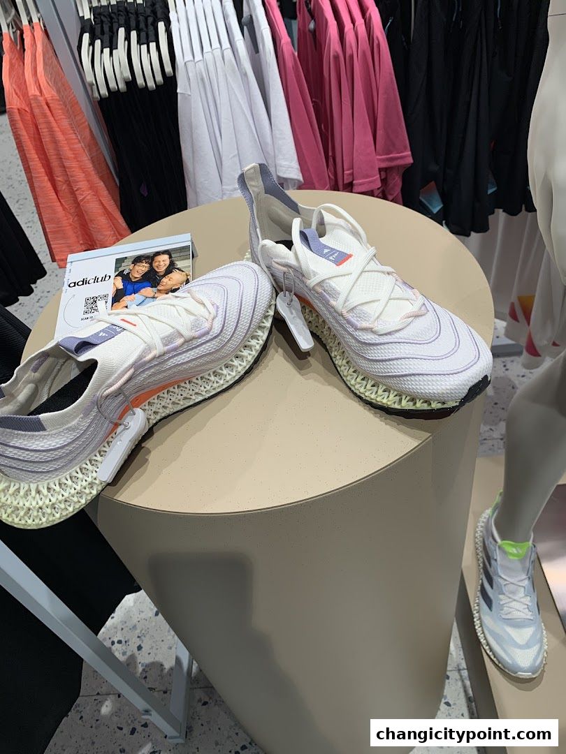 Adidas shoes displayed on a table with clothing in the background.