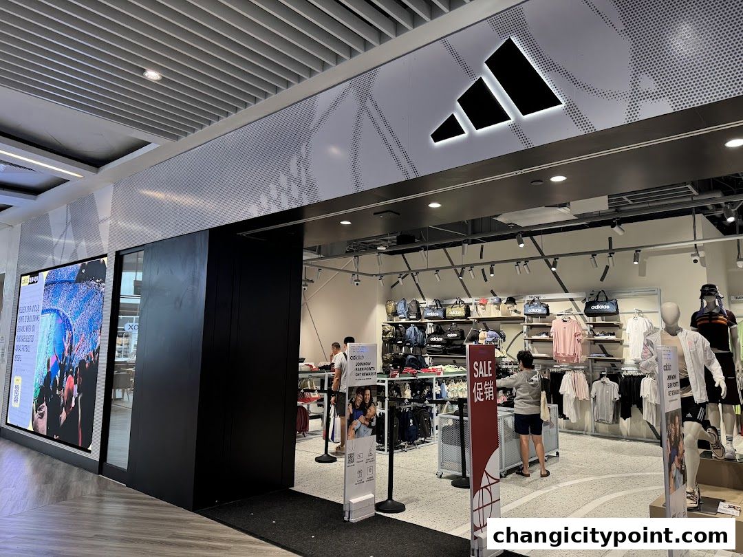 Adidas Factory Outlet store entrance with merchandise displayed inside and a large digital screen.