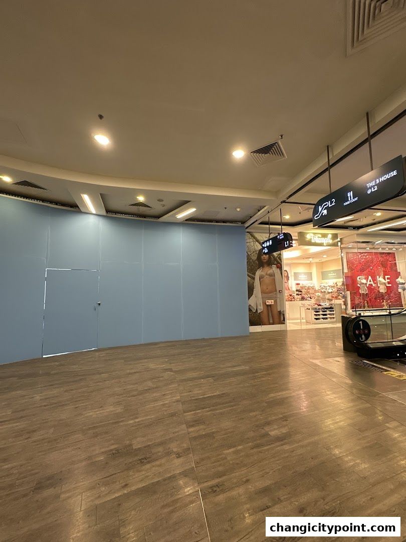 Interior view of a shopping mall with a blue wall and a glimpse of a store with a sale sign.