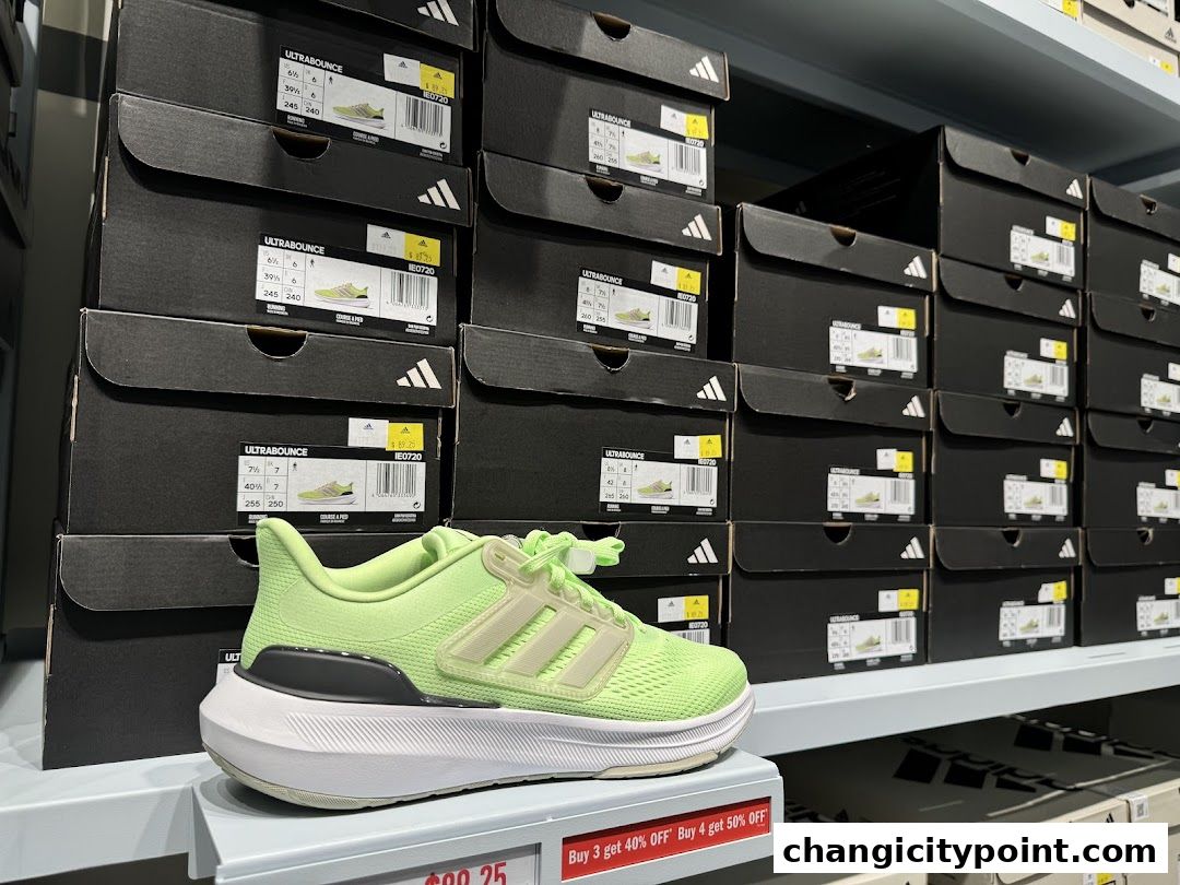 A bright green Adidas Ultrabounce shoe displayed in front of stacks of shoe boxes.