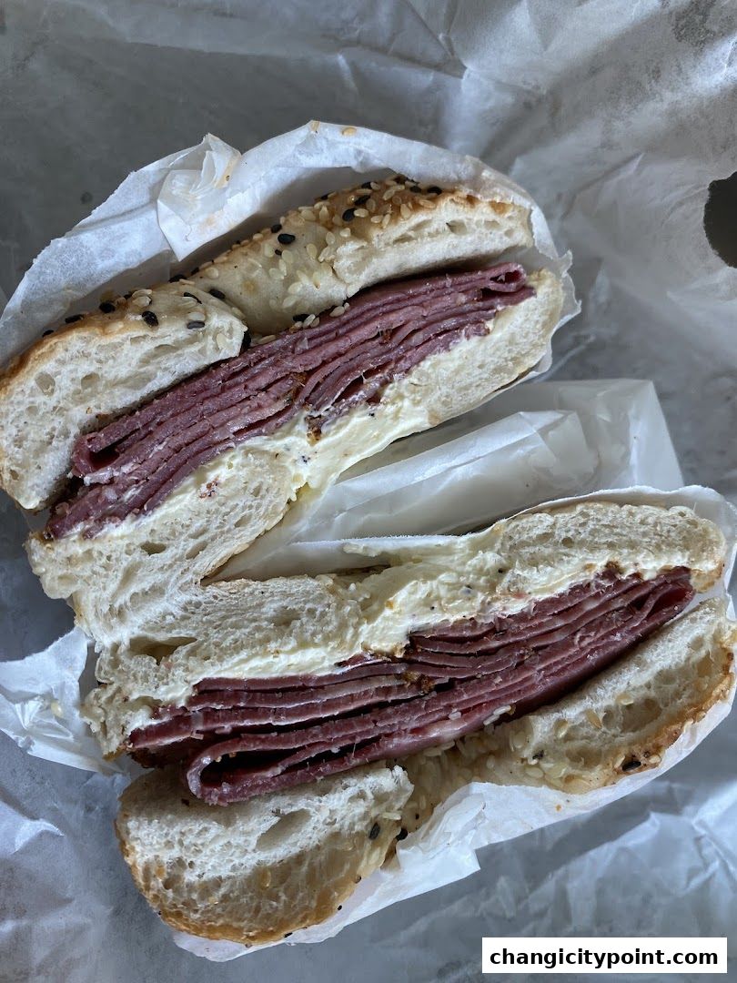 A delicious bagel sandwich with thinly sliced meat and cream cheese, wrapped in paper.