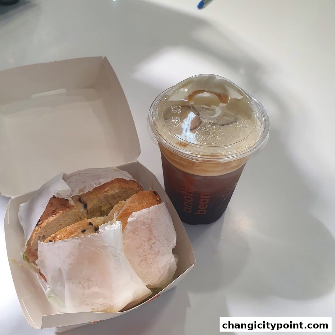 A bagel sandwich in a box next to an iced coffee from 'another bean'.