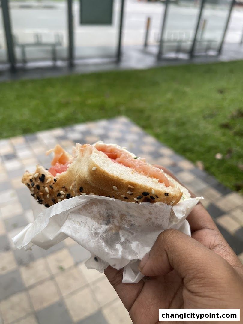 A hand holds a sesame seed bagel sandwich with salmon and cream cheese.