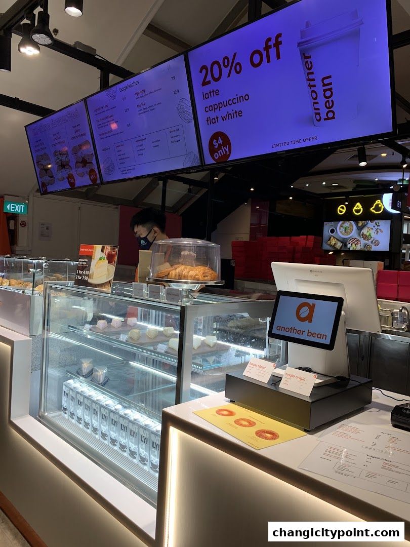 A coffee shop counter with pastries, drinks, and digital menus displaying promotions.