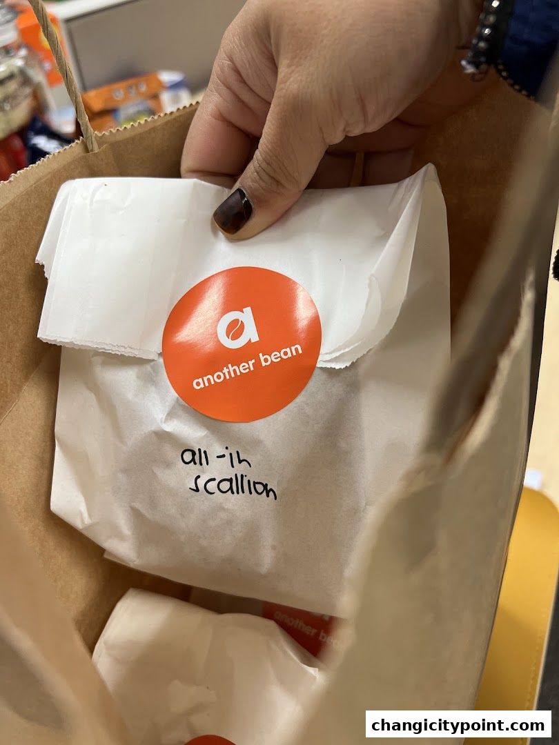 A hand holding a paper bag with a white paper-wrapped item from 'another bean'.