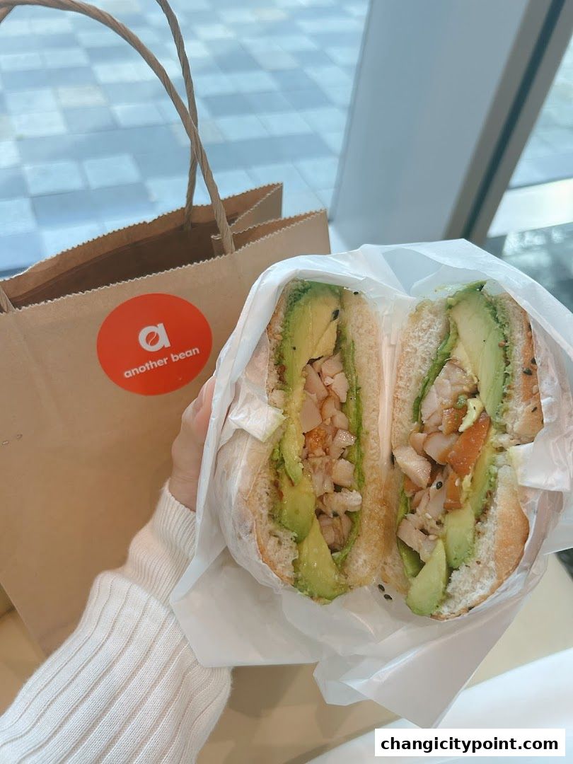 A person holds a delicious avocado and chicken sandwich from another bean.