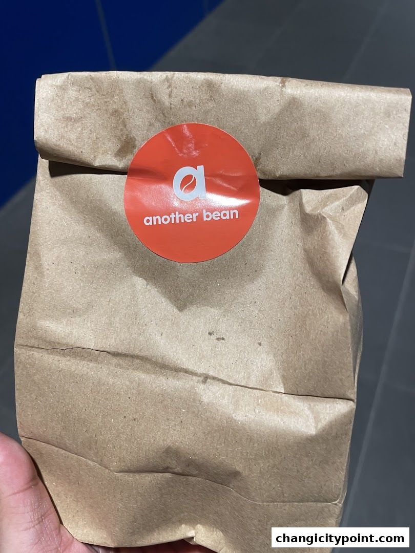 A brown paper bag with the 'another bean' logo sticker on it.