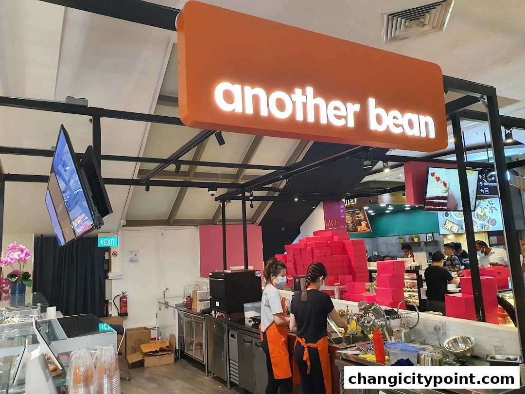 Interior view of 'another bean' cafe with staff preparing drinks and displaying cakes.