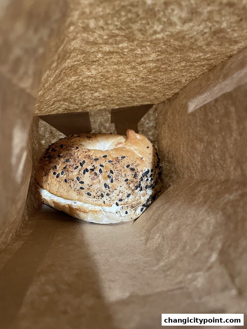 A delicious bagel with cream cheese peeking out of a paper bag.