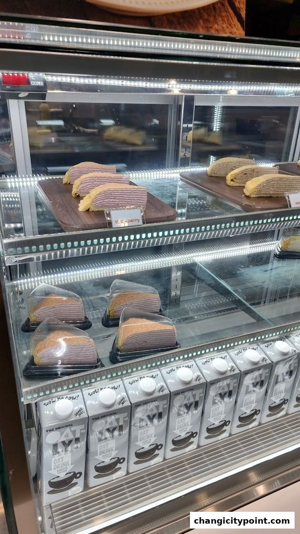 A display case filled with layered cakes and Oatly oat milk cartons.