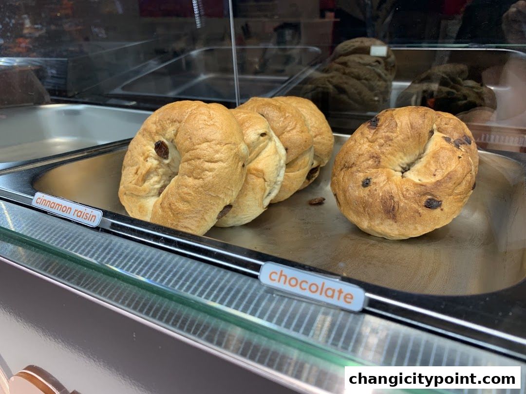 Freshly baked cinnamon raisin and chocolate bagels displayed in a bakery case.