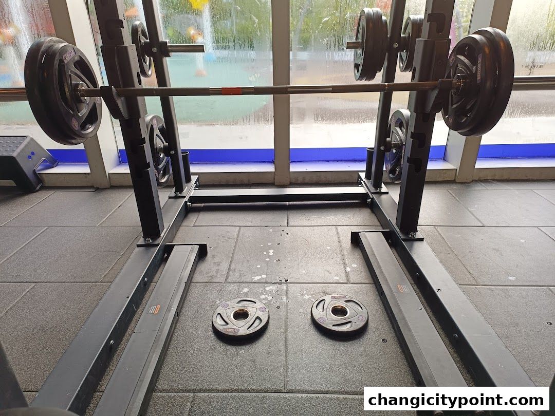 A squat rack with weights loaded and plates on the floor in a gym.