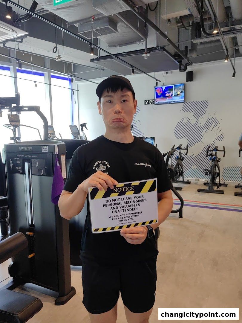 A man holds a notice sign in a gym with exercise equipment in the background.