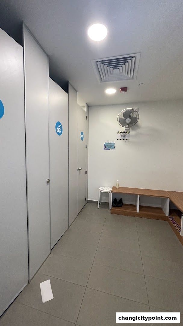 Interior view of a gym's changing room with lockers, bench, and fan.