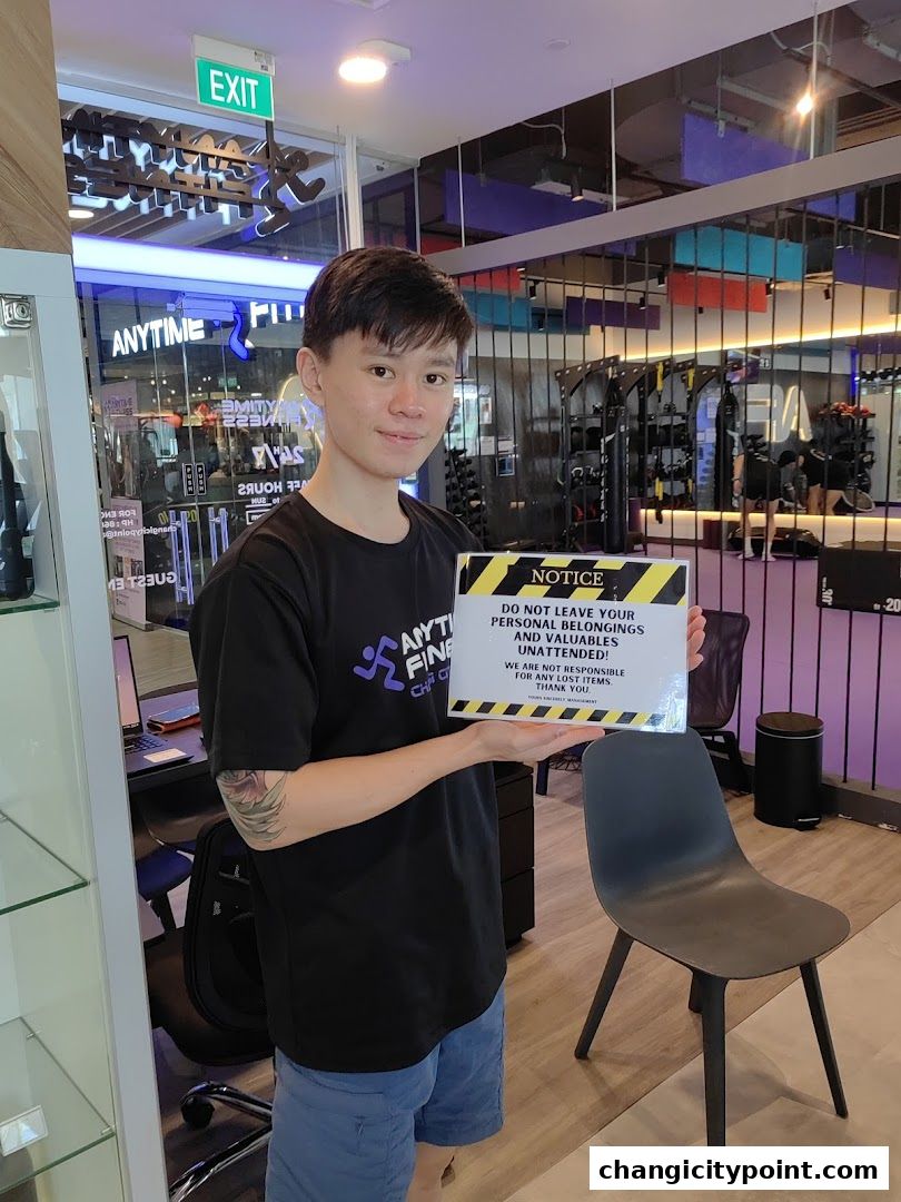 A man holds a notice sign inside Anytime Fitness Changi, with gym equipment visible.
