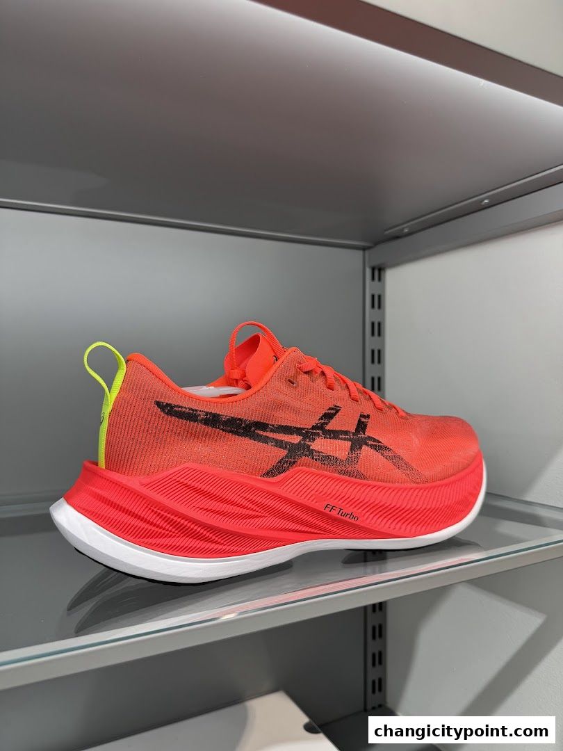 A bright orange ASICS running shoe with black accents is displayed on a shelf.