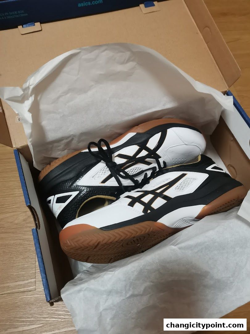 A pair of white and black ASICS athletic shoes are displayed in their original box.