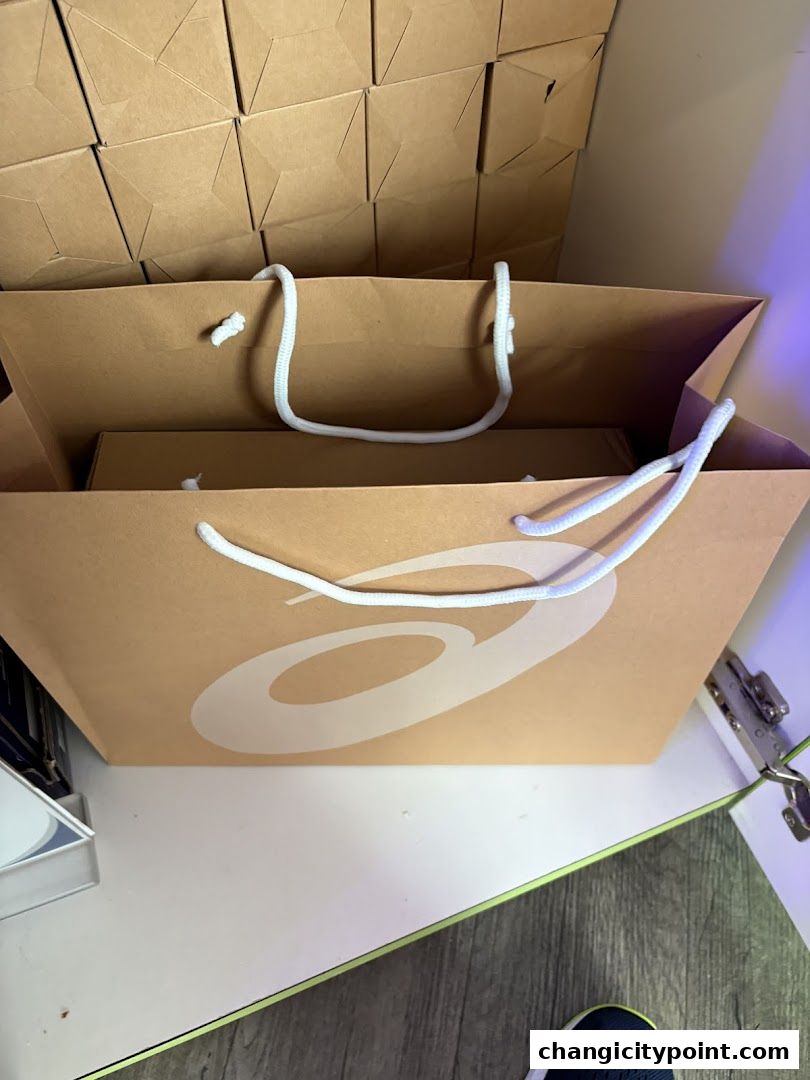 ASICS shopping bag with a box inside, stacked brown boxes in the background.