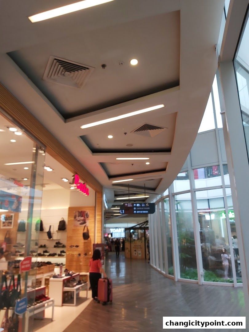 A woman with a pink suitcase walks down a mall corridor past a Bata shoe store.