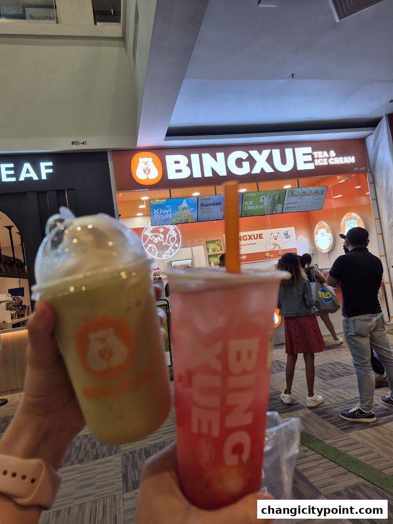 Two refreshing drinks from BingXue Tea & Ice Cream are held up in front of the shop.