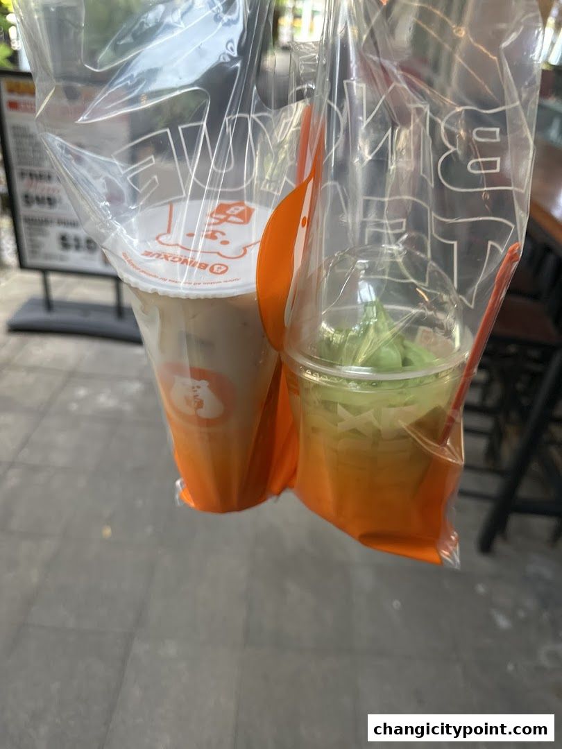 Two takeaway drinks from BingXue Tea Ice Cream, one with milk tea and another with green soft serve.
