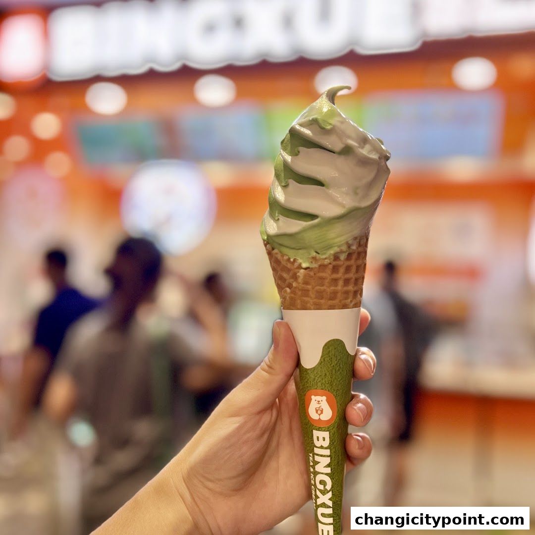 A hand holds a swirled green and white ice cream cone with the BingXue logo.