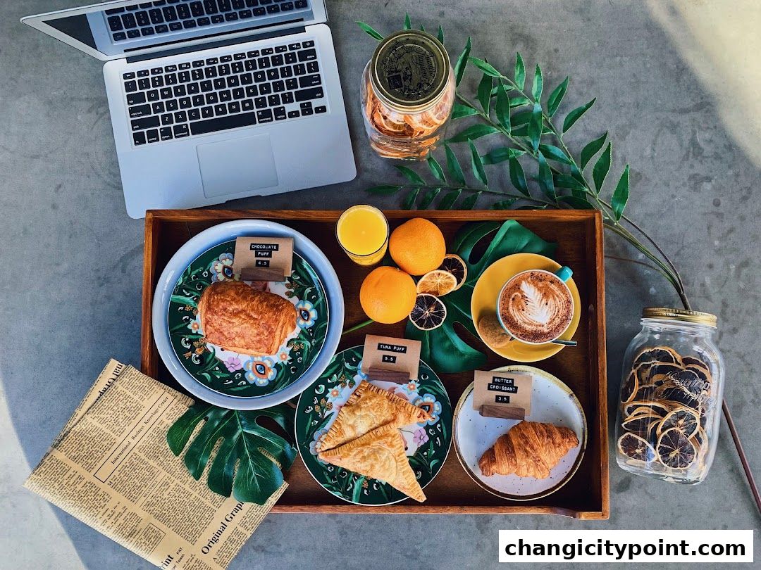 A tray with pastries, coffee, orange juice, and a laptop, suggesting a work-from-cafe setting.