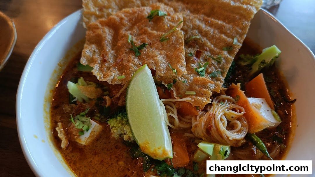 A close-up of a delicious bowl of curry noodles with vegetables and crispy toppings.