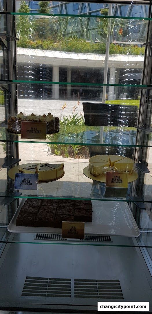 A display case filled with various cakes and brownies, with a lush green background.