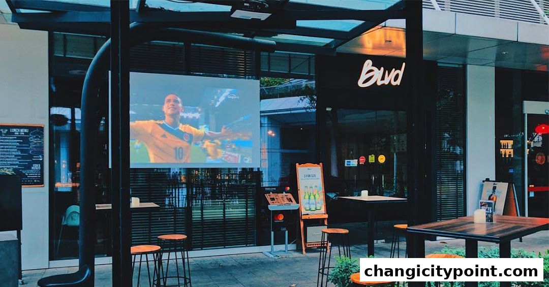 Outdoor seating area of a bar with a projector screen showing a soccer match.
