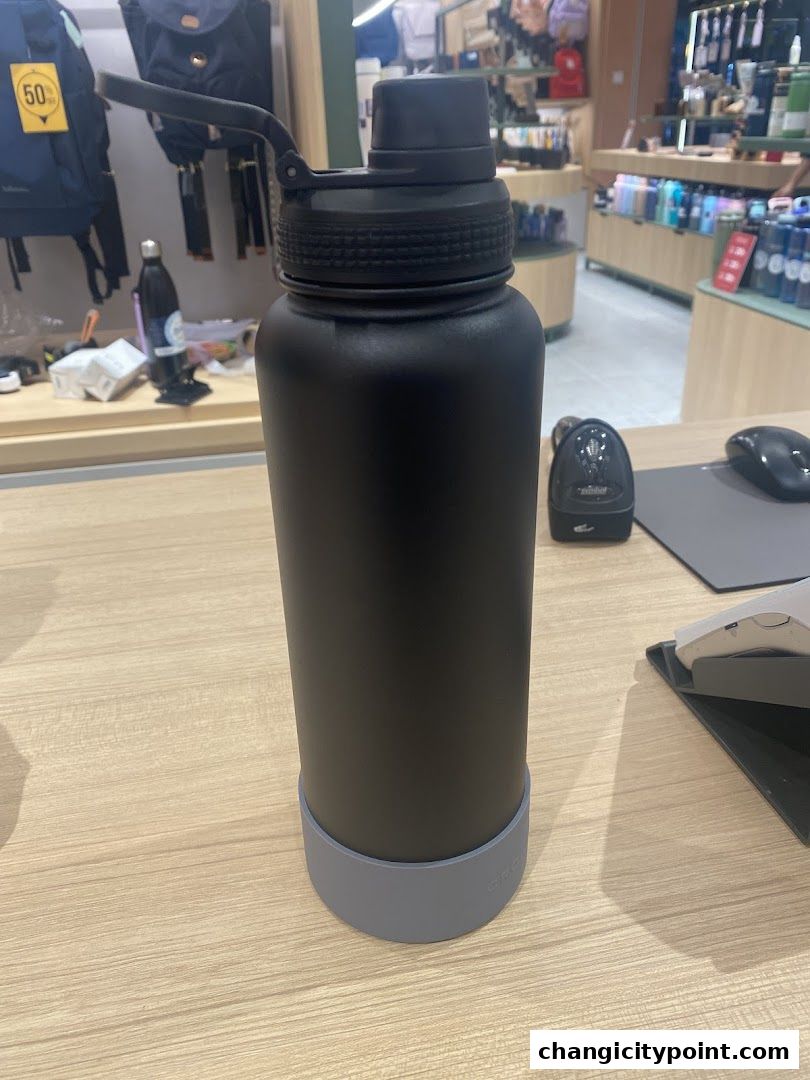 A black water bottle with a grey base sits on a wooden counter in a retail store.