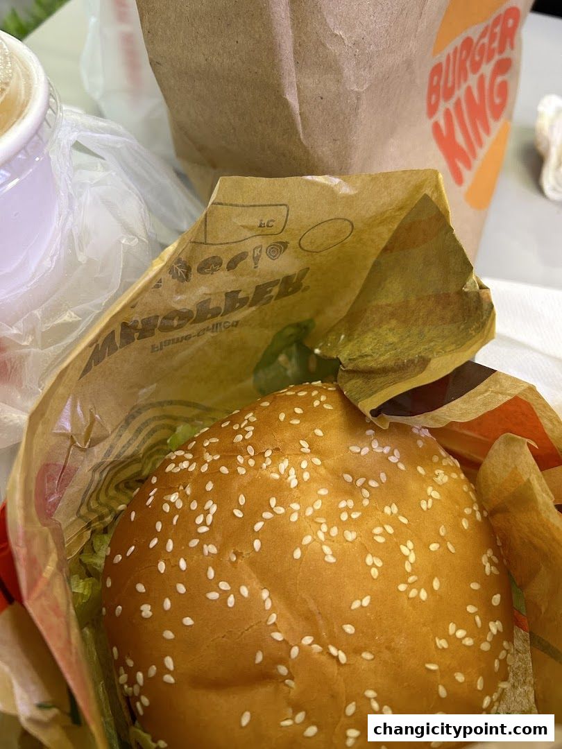 A close-up of a Burger King Whopper burger in its wrapper with a drink and bag.