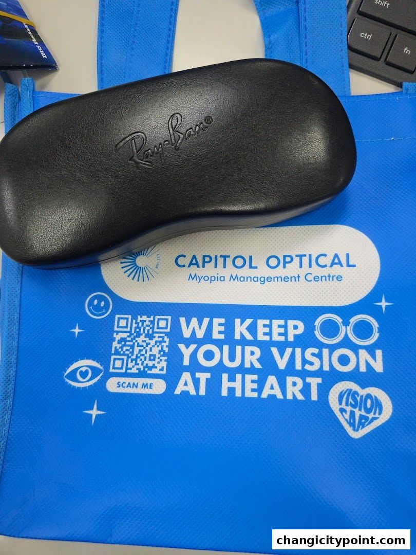 A blue tote bag from Capitol Optical with a Ray-Ban glasses case on top.
