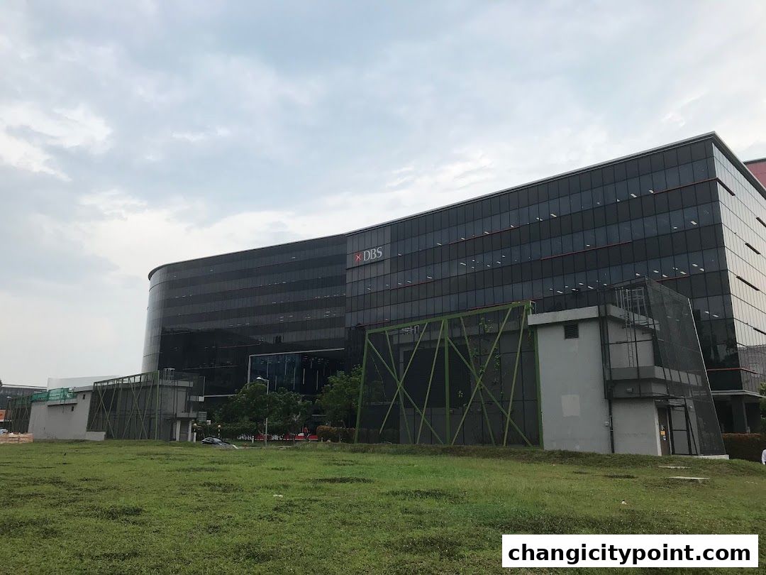 A modern glass-fronted building with the DBS logo visible under a cloudy sky.