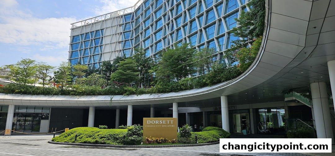 The modern entrance of Dorsett Changi City Singapore with lush greenery and a curved canopy.