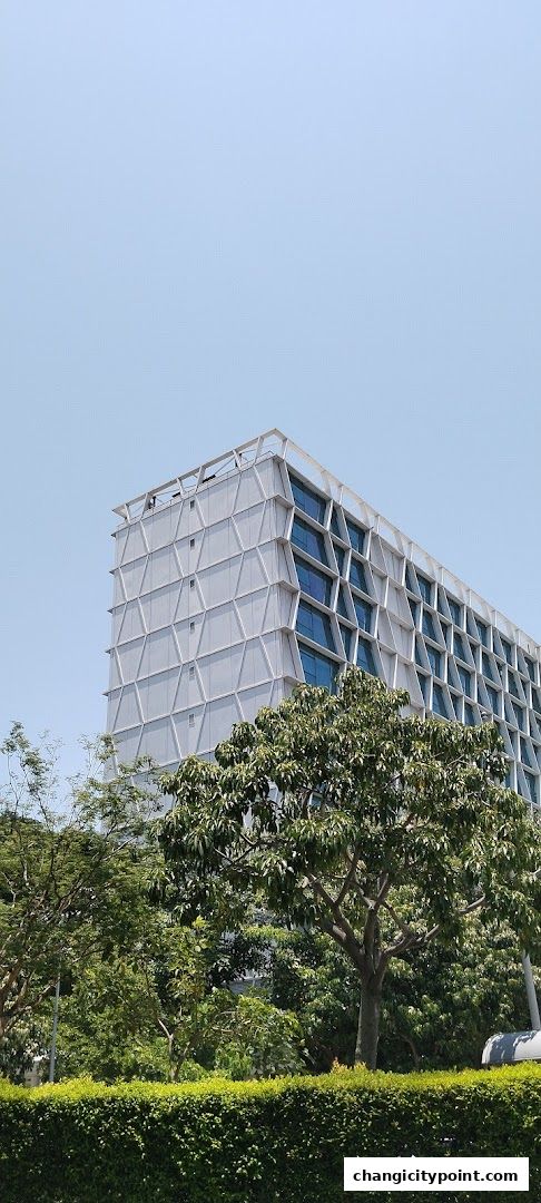 Modern building with geometric facade and lush green trees in foreground.