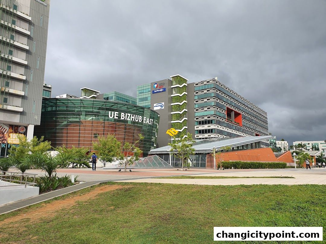 Modern office buildings and a green space under a cloudy sky.