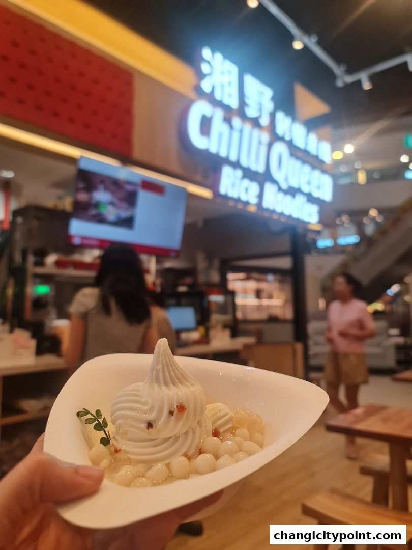 A hand holds a dessert with white swirls and small white balls in a white bowl.