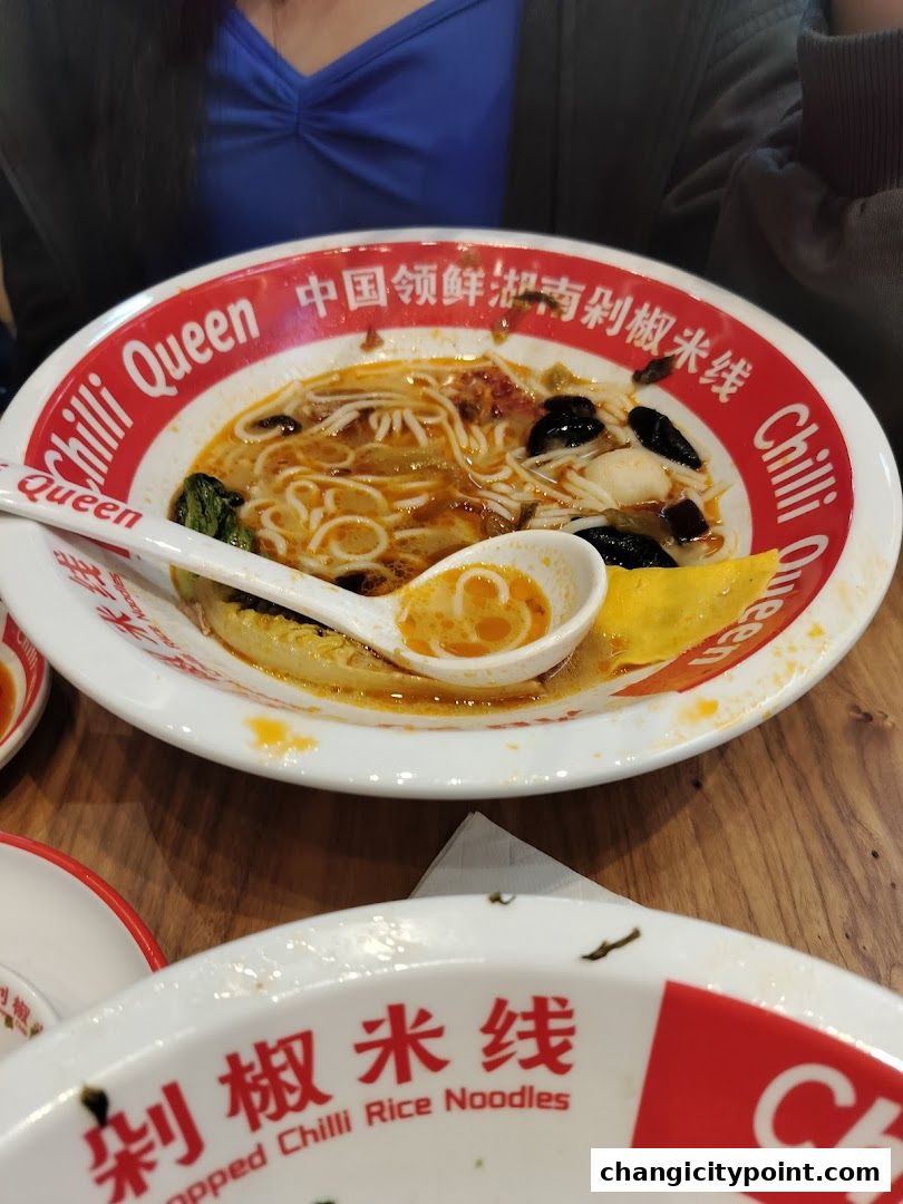 A close-up of a bowl of spicy rice noodles with a spoon and another bowl in the foreground.