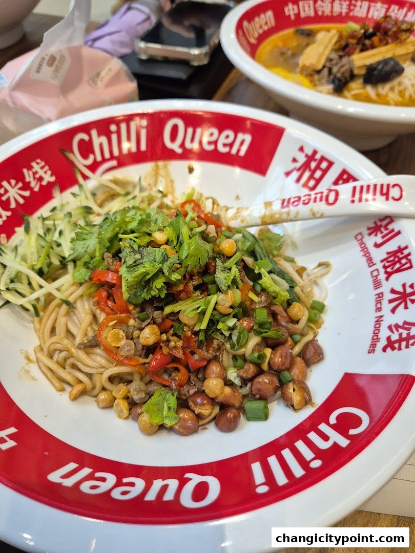 A close-up of a bowl of chopped chili rice noodles with toppings and a spoon.