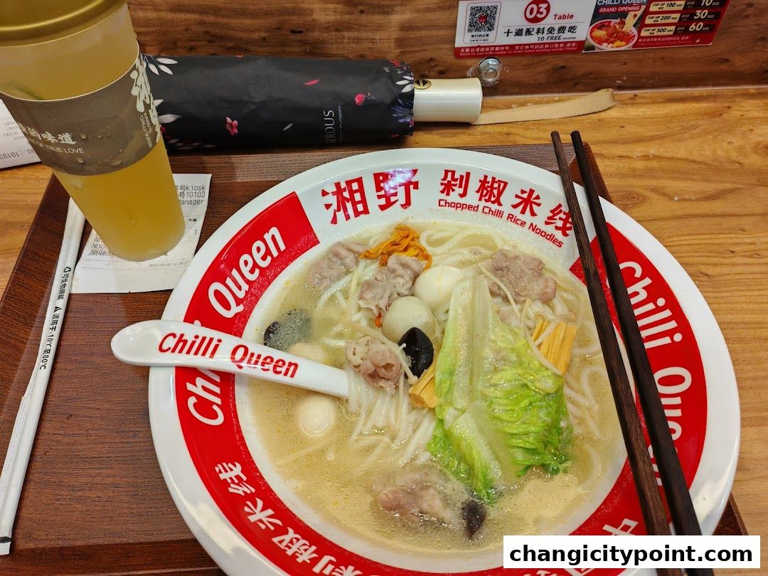 A bowl of chopped chili rice noodles with meat, vegetables, and a drink.