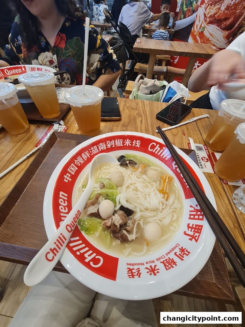 A bowl of rice noodles with meat and vegetables, served with drinks.