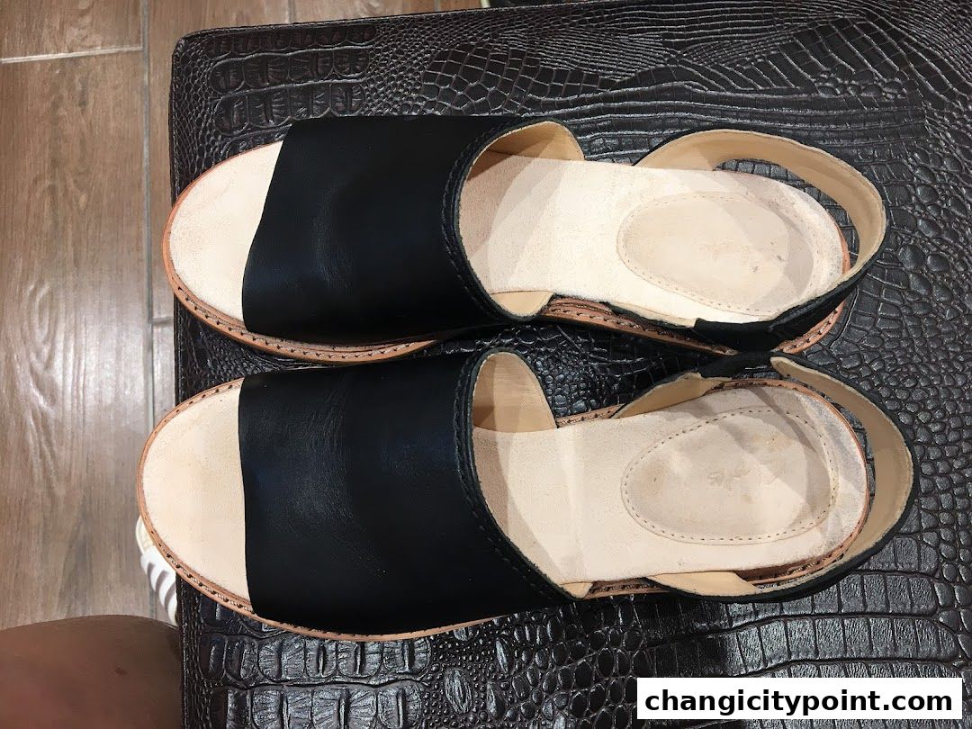 A pair of black leather sandals with tan soles and straps, displayed on a textured surface.