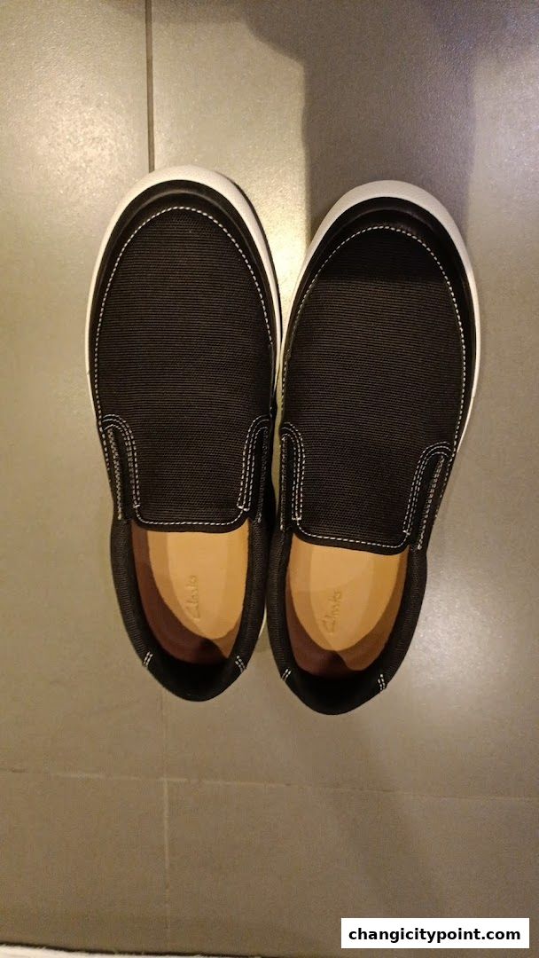 A pair of black slip-on shoes with white stitching and tan insoles from Clarks.