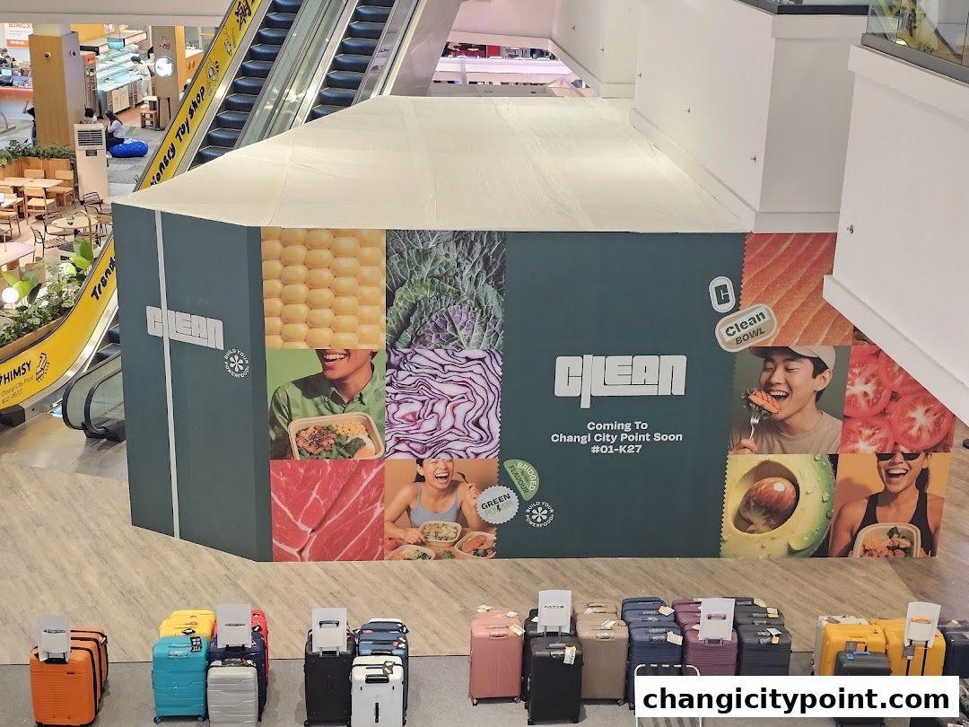 A temporary construction hoarding for a 'CLEAN SALAD BAR' shop with images of fresh ingredients and happy customers.