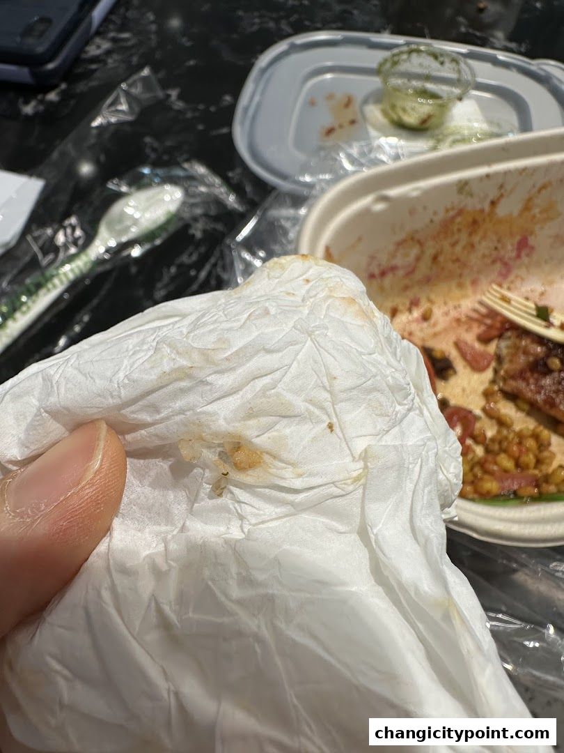 A hand holding a used napkin over a table with leftover food containers.